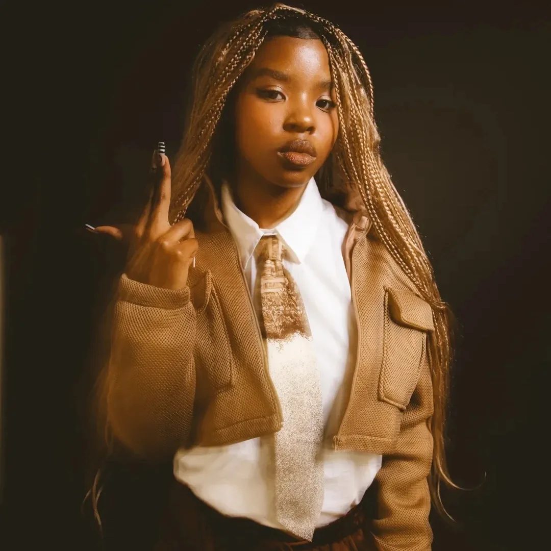 Glockie in a tan jacket, shirt and tie, hand raised