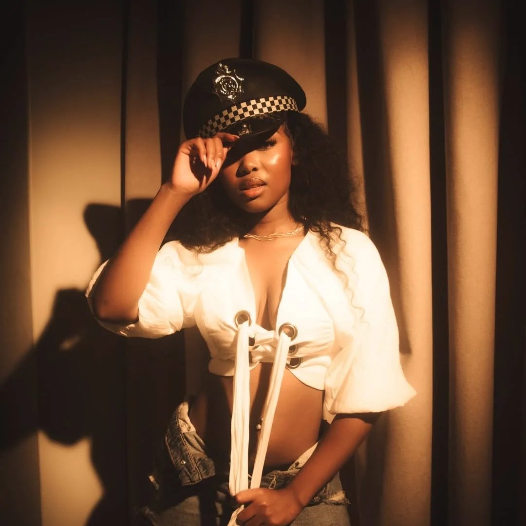 Miss Lyra in a police-style cap and white blouse